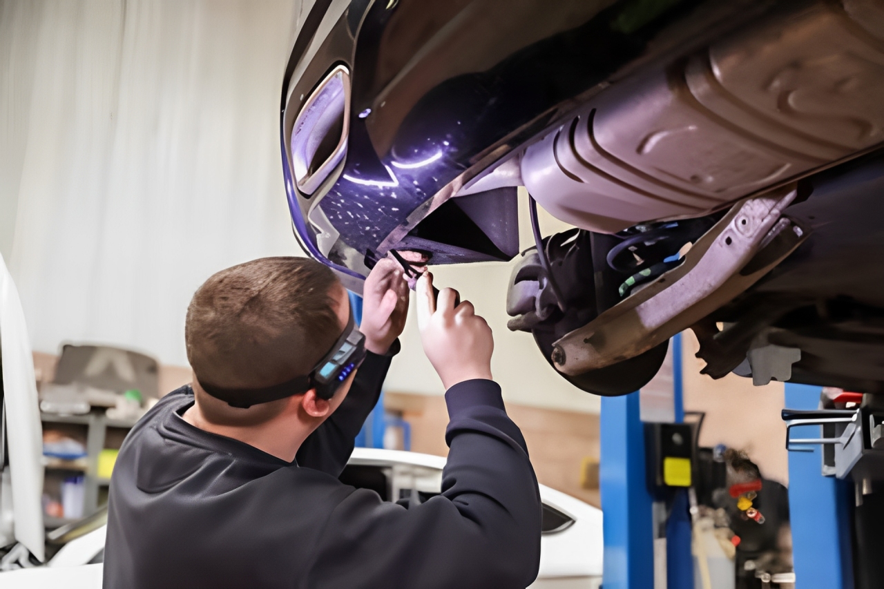 Mechanic wearing headlamp works on the undercarriage of a dark-colored car.
