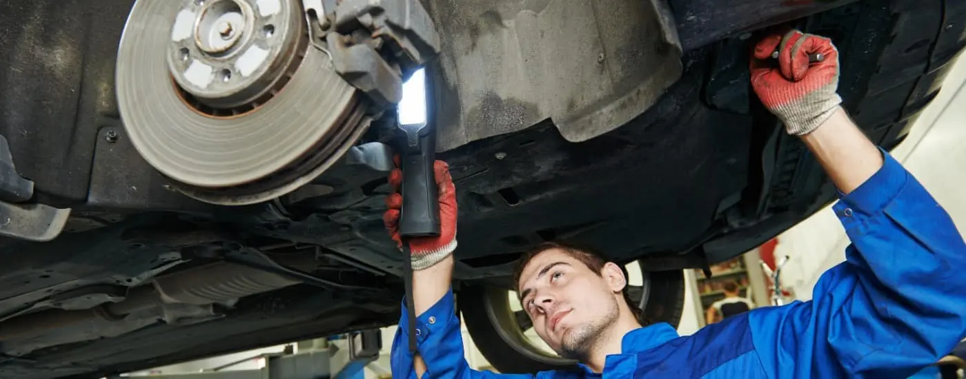 Mechanic working underneath a car, inspecting the brake disc and suspension.