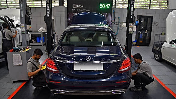 Rear view of a blue Mercedes-Benz E-Class in a service bay with technicians.