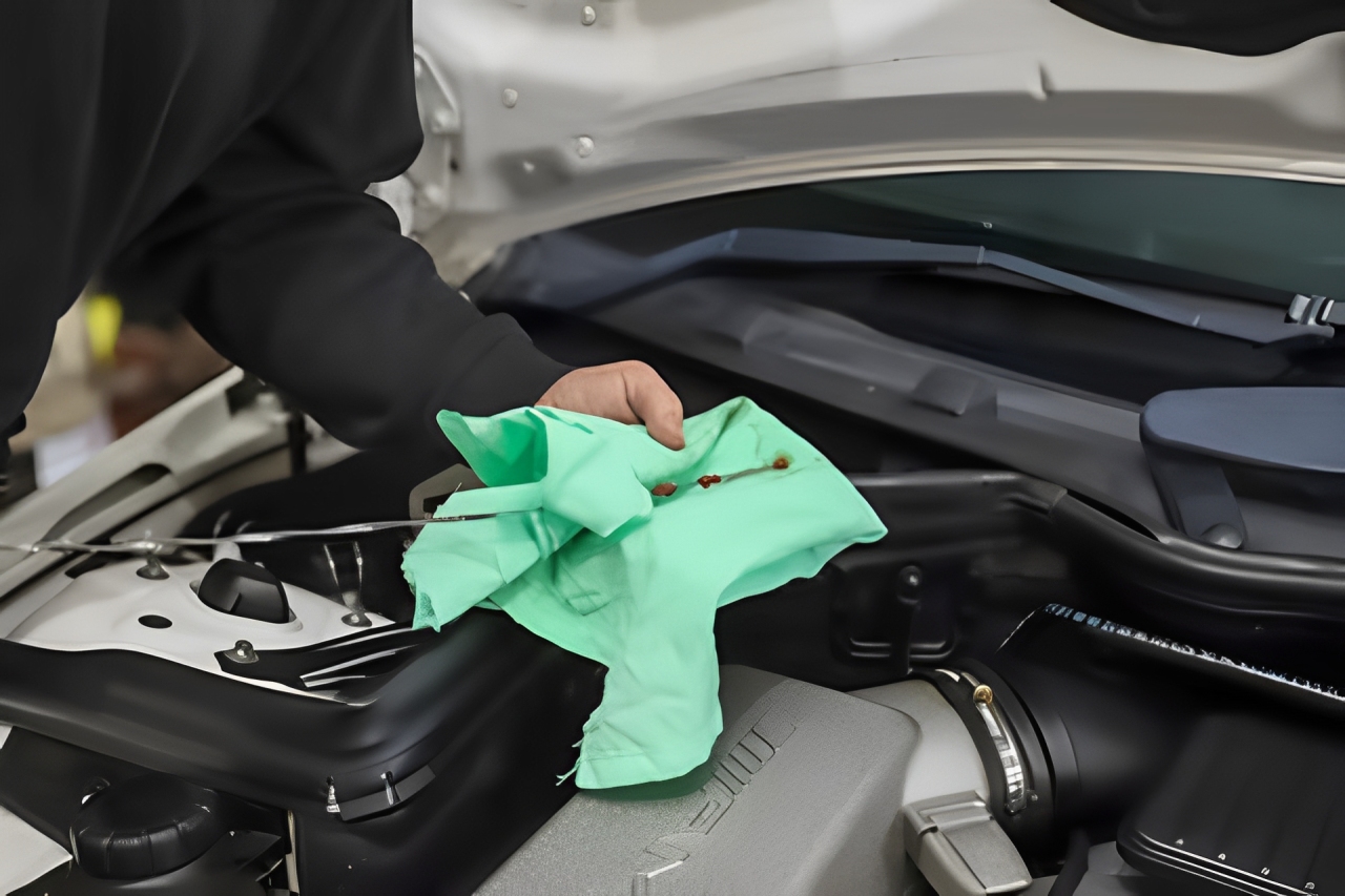 A hand wipes the engine bay of a Mercedes-Benz with a green cloth.