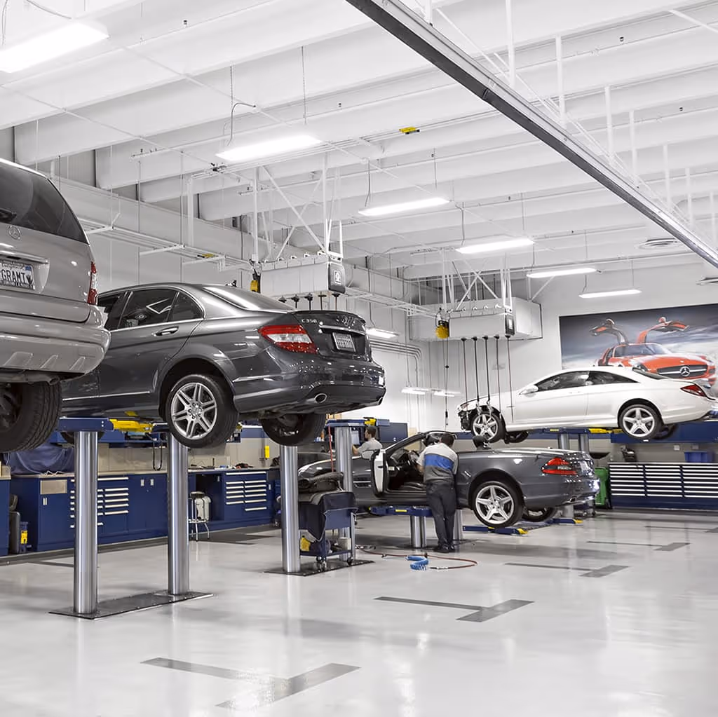 Several Mercedes-Benz cars on lifts in a bright, modern service center.