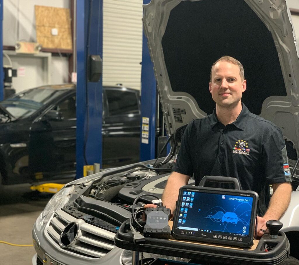 Mechanic stands with diagnostic equipment in front of a Mercedes-Benz with an open hood.
